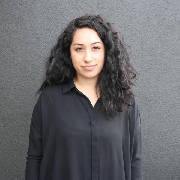 A woman looking at the camera wearing a black shirt, and a black wall behind